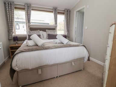 A bedroom with a bed with rolled towels pillows and bedside tables with lamps at Lodge 4 in St Asaph