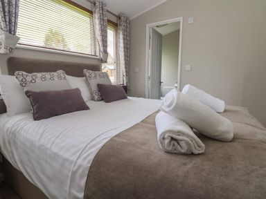 A bedroom with a bed made with white and beige bedding and rolled towels on the bed at Lodge 4 in St Asaph