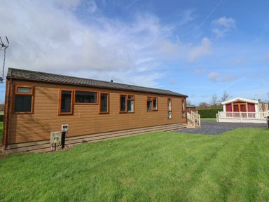 A brown mobile home with several windows on a grassy lawn next to another mobile home at Lodge 4 in St Asaph
