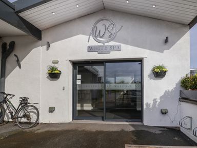 The entrance to White Spa with automatic glass doors a bicycle parked to the left and flower pots mounted on the wall at Lodge 4 in St Asaph