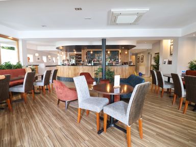 A dining area with tables and chairs facing a wooden bar with bottles at Lodge 4 in St Asaph