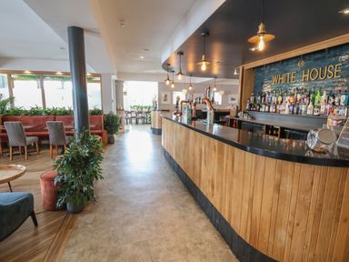 A bar with wooden panels and bottles on shelves behind it next to a seating area with chairs and plants at Lodge 4 in St Asaph