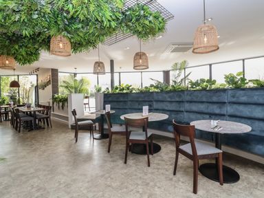 A dining area with round tables wooden chairs and green plants indoors at Lodge 4 in St Asaph