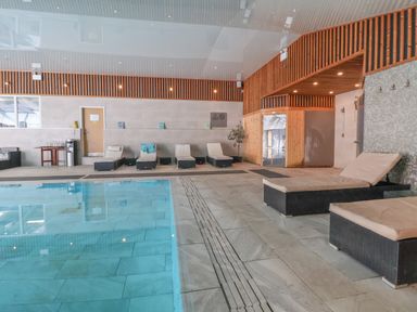 An indoor swimming pool with lounge chairs along the wall and a wooden paneled sauna at Lodge 4 in St Asaph