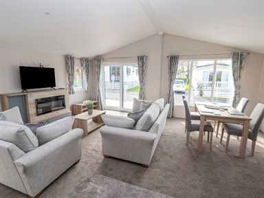 A living room with two grey sofas a wooden coffee table a wall mounted TV and a dining table with four chairs at Lodge 9 in St Asaph