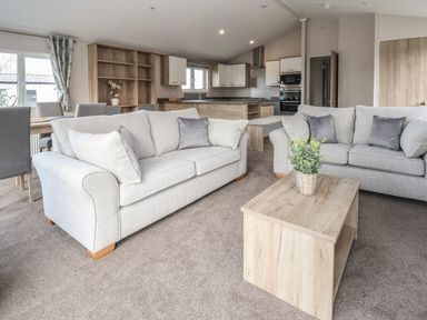 A living room with two grey sofas a wooden coffee table and an open kitchen area at Lodge 9 in St Asaph