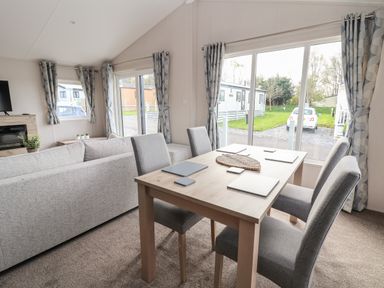 A dining area with a table and four chairs next to large windows showing outside caravans and a car at Lodge 9 in St Asaph