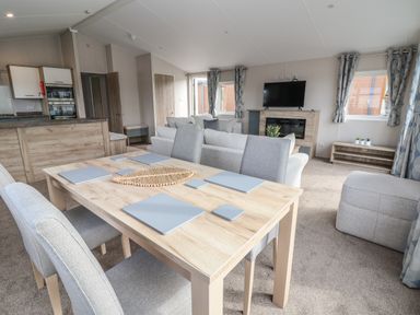 A dining table with four chairs in an open plan living room with a sofa TV and kitchen at Lodge 9 in St Asaph