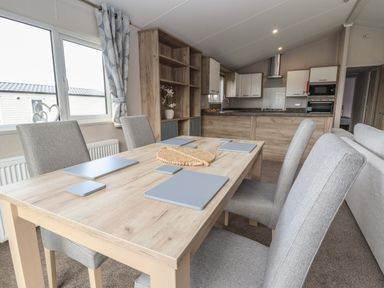 A dining area with a wooden table and four grey chairs next to a kitchen with cabinets and appliances at Lodge 9 in St Asaph