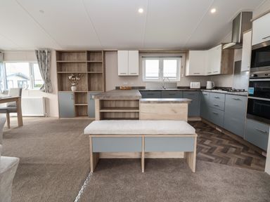 A kitchen with blue and wood cabinets a window a built in oven and a cushioned bench at Lodge 9 in St Asaph