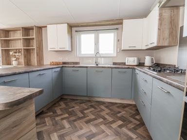 A kitchen with blue lower cabinets and white upper cabinets a gas stove a toaster and a kettle on the countertop at Lodge 9 in St Asaph