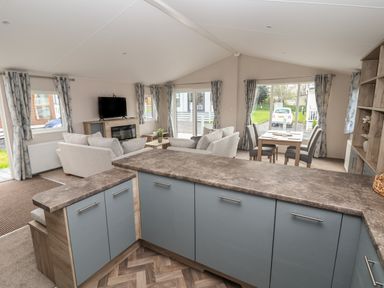 An open living space with a kitchen counter, sofas, a TV, dining table, and windows with curtains at Lodge 9 in St Asaph