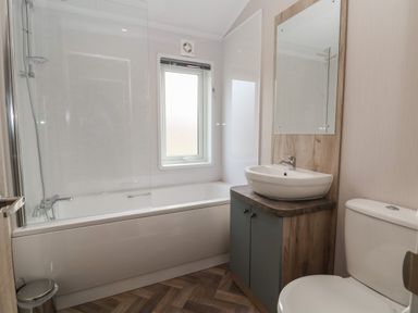 A bathroom with a bathtub shower combination a sink with a mirror and a toilet at Lodge 9 in St Asaph