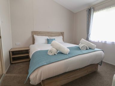 A bedroom with a double bed white linens blue runner rolled towels and a bedside table at Lodge 9 in St Asaph