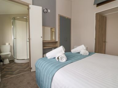 A bedroom with a bed and towels near a bathroom with a shower at Lodge 9 in St Asaph