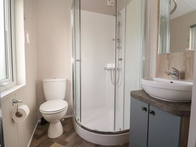 A bathroom with a toilet a corner shower enclosure and a sink on a cabinet at Lodge 9 in St Asaph