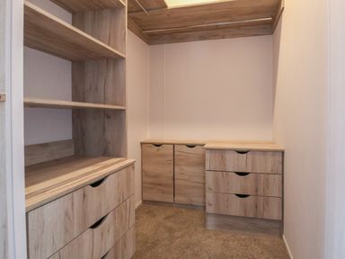 A walk-in closet with wooden shelves drawers and hanging rods at Lodge 9 in St Asaph