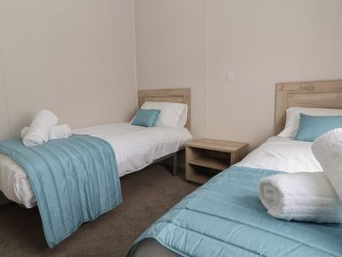A bedroom with two single beds with blue throws and pillows and a wooden bedside table at Lodge 9 in St Asaph