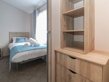 A bedroom with a single bed and blue bedding next to a wooden chest of drawers at Lodge 9 in St Asaph