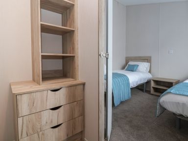 A bedroom with two single beds blue bed runners wooden bedside table and wooden chest of drawers at Lodge 9 in St Asaph