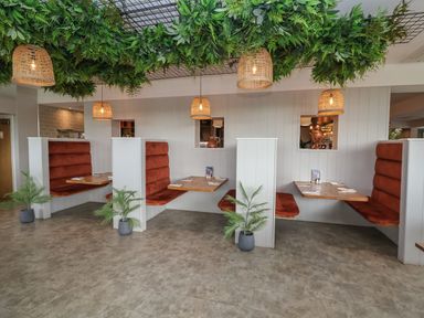 A dining area with orange upholstered booth seating wooden tables hanging wicker lamps and plants at Lodge 9 in St Asaph