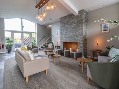 A sitting area with sofas and armchairs around a stone fireplace at Lodge 9 in St Asaph