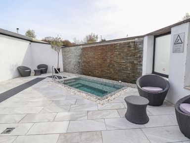 An outdoor patio area with a small pool surrounded by stone tiles and wicker chairs at Lodge 9 in St Asaph