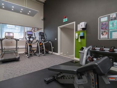 A gym room with exercise machines dumbbells a bench and a bulletin board at Lodge 9 in St Asaph