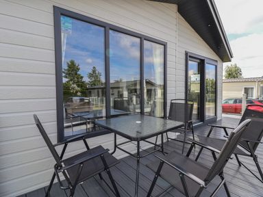An outdoor patio with a glass table and four black chairs outside a house at Lodge 9 in St Asaph