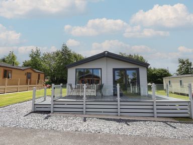 A single story house with a patio deck and glass railing at Lodge 9 in St Asaph