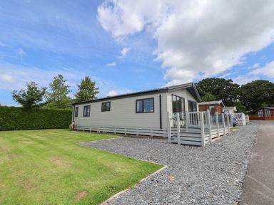 A mobile home with a gravel driveway and grass lawn surrounded by trees at Lodge 9 in St Asaph