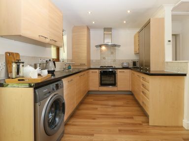 A kitchen with wooden cabinets black countertops a washing machine an oven a stove and a sink at Ty Gareg in Llanddaniel near Gaerwen