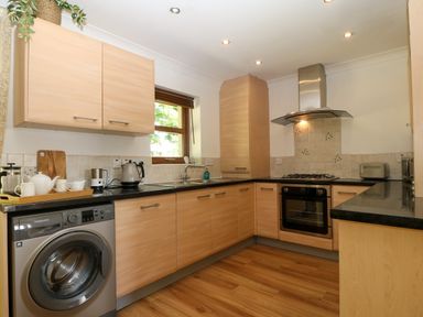 A kitchen with wooden cabinets a washing machine an oven a gas stove and a sink at Ty Gareg in Llanddaniel near Gaerwen