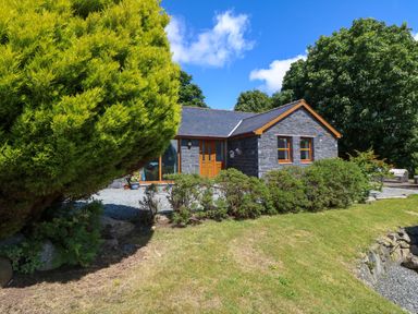 A stone house with wooden doors and windows surrounded by trees and bushes at Ty Gareg in Llanddaniel near Gaerwen