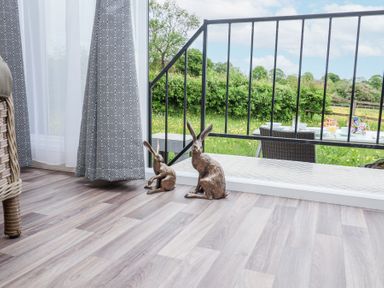 Two rabbit sculptures on a wooden floor next to a glass door with gray patterned curtains and an outdoor patio with a table and chairs at The Hoot in Great Finborough near Stowmarket