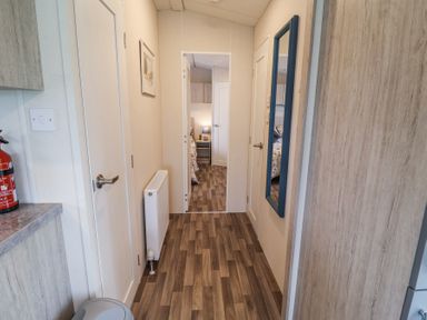 A hallway with wood flooring a radiator a wall mirror and doors leading to other rooms at The Hoot in Great Finborough near Stowmarket