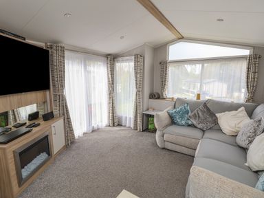 A living room with a sectional sofa cushions curtains and a TV above a fireplace at Woodlands Lodge in Bontuchel near Ruthin