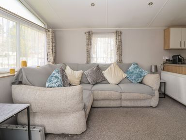 A living room with a patterned sofa and multiple cushions near windows with curtains at Woodlands Lodge in Bontuchel near Ruthin