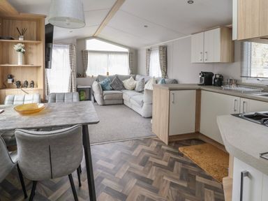 An open living and kitchen area with a dining table and chairs a corner sofa with cushions kitchen cabinets and appliances at Woodlands Lodge in Bontuchel near Ruthin