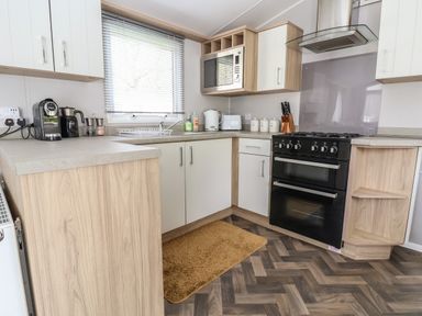 A kitchen with a black oven, microwave, kettle, toaster, coffee machine, and wooden cabinets at Woodlands Lodge in Bontuchel near Ruthin