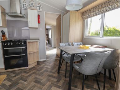 A kitchen with a black oven and a dining table with gray chairs near a window at Woodlands Lodge in Bontuchel near Ruthin