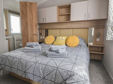 A bedroom with a bed with gray patterned bedding and yellow pillows and towels on the bed at Woodlands Lodge in Bontuchel near Ruthin