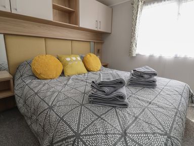 A bedroom with a patterned bedspread and folded towels on the bed at Woodlands Lodge in Bontuchel near Ruthin