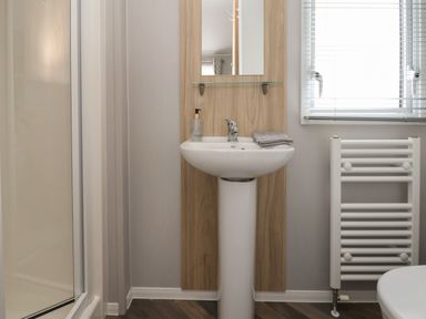 A bathroom with a pedestal sink a mirror and shelf a towel radiator and a window with blinds at Woodlands Lodge in Bontuchel near Ruthin