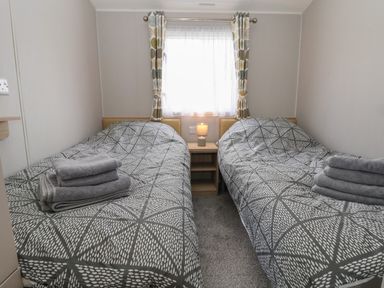 A bedroom with two single beds grey patterned bedding and folded towels on each at Woodlands Lodge in Bontuchel near Ruthin