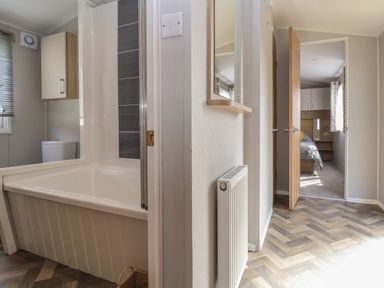 A bathroom with a bathtub and toilet connected to a hallway leading to a bedroom at Woodlands Lodge Bontuchel near Ruthin