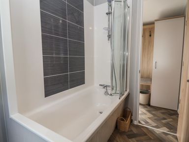 A bathroom with a bathtub shower combination and basket on the floor at Woodlands Lodge in Bontuchel near Ruthin