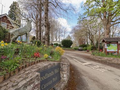 A road entrance with a stone wall sign for Woodlands Hall Caravan Park a statue of a stag flowers trees and a map board at Woodlands Lodge in Bontuchel near Ruthin