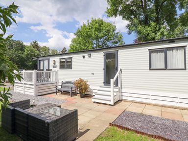 An exterior view of a white mobile home with a small porch and outdoor seating in a garden at Woodlands Lodge in Bontuchel near Ruthin