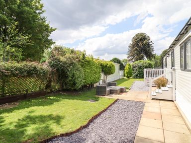 An outdoor area with patio flooring seating and grass next to white mobile homes at Woodlands Lodge in Bontuchel near Ruthin